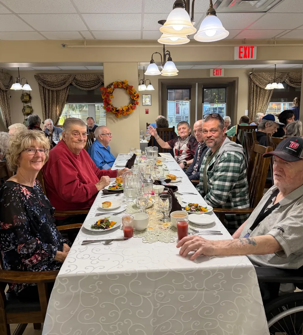 Residents and guests smiling along a long table during Thanksgiving dinner at Parkview