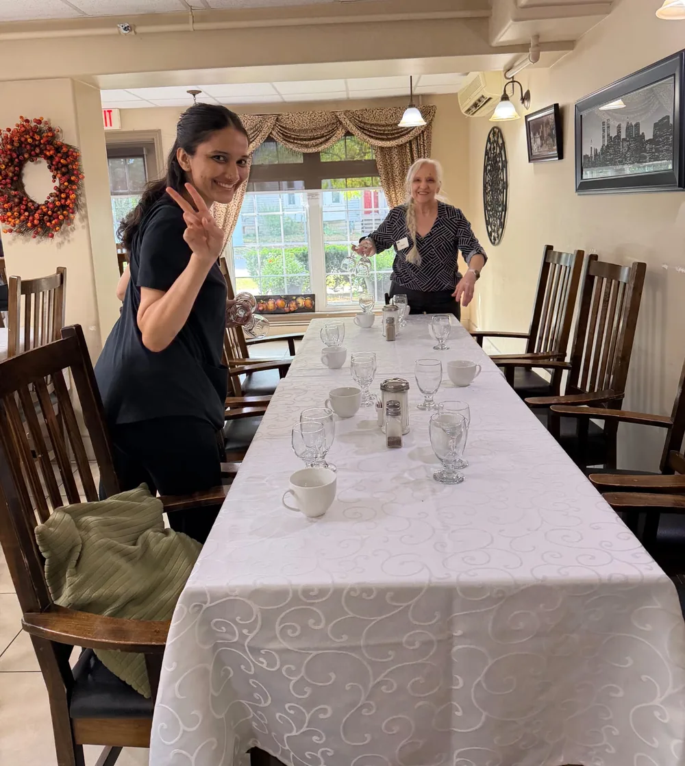 Two staff members smiling while setting glasses on a long table before Thanksgiving dinner