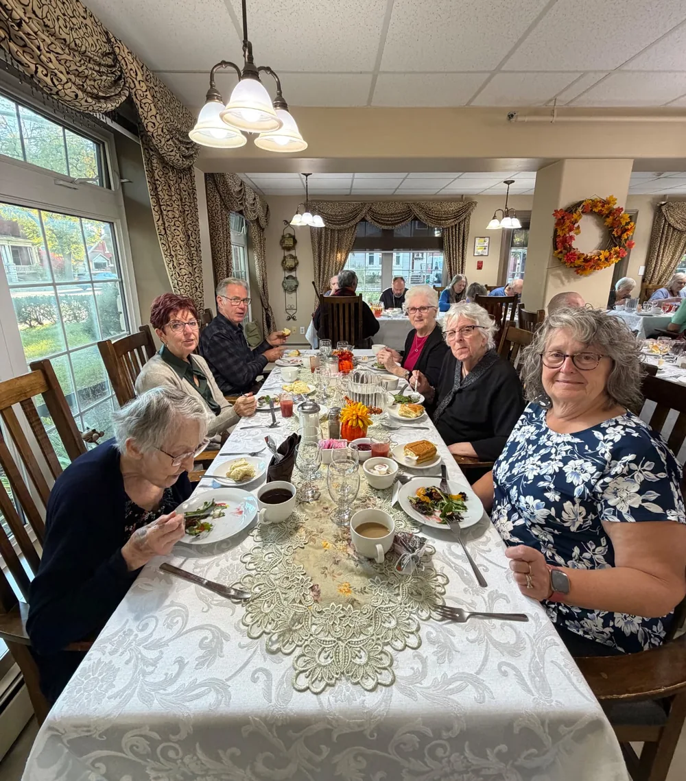 Six residents and guests sharing Thanksgiving dinner at a table beside the window