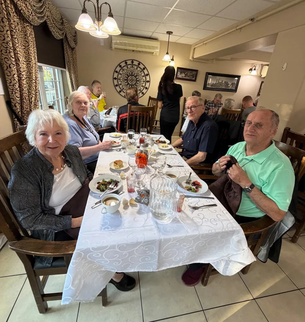 Four residents seated at a dinner table smiling at the camera during Thanksgiving dinner