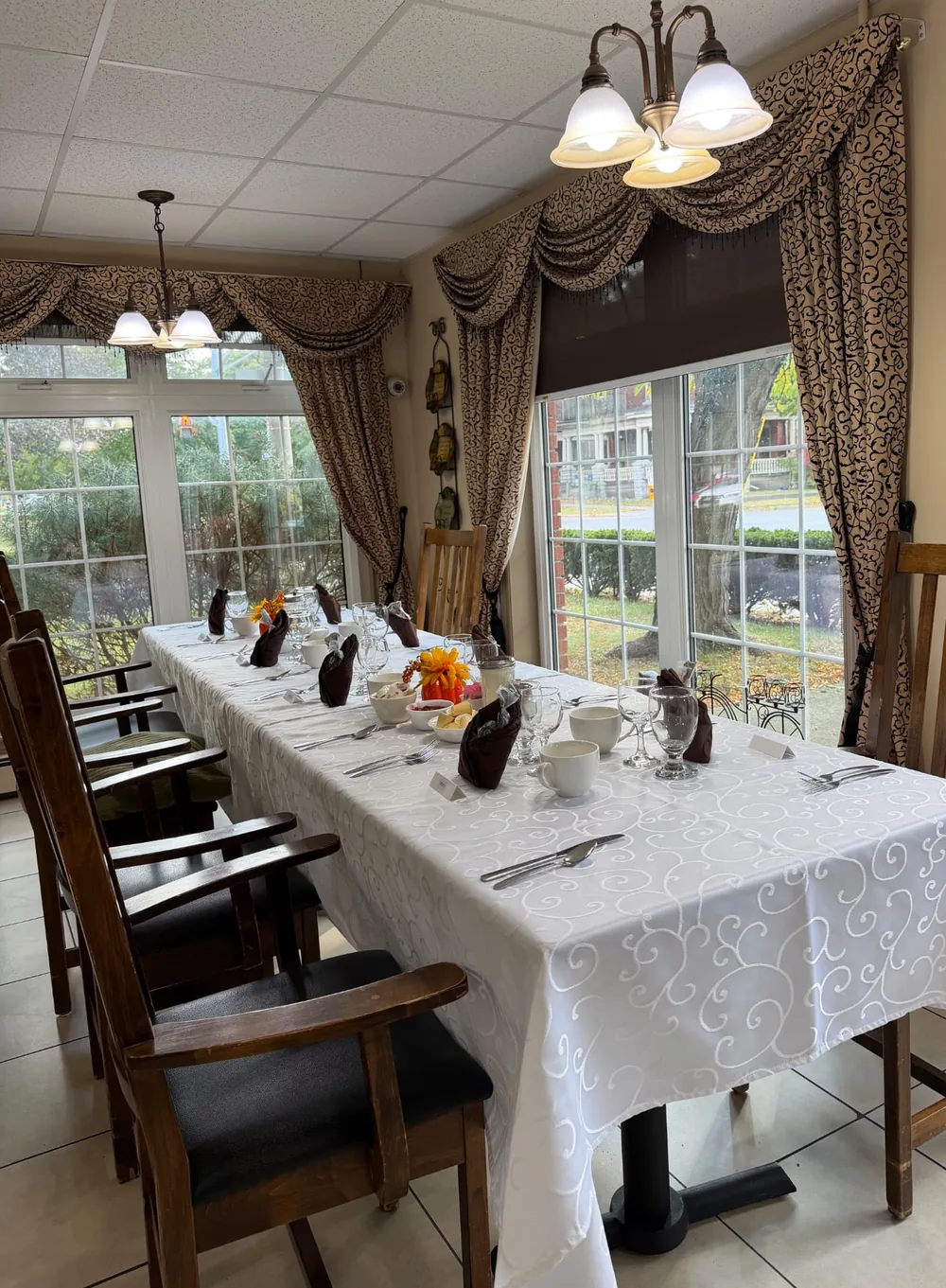 Long table set with white linen, brown napkins and pumpkin centrepieces beside large windows